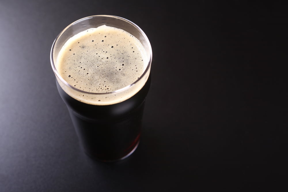 Nonic pint glass full of dark stout ale over a dark background