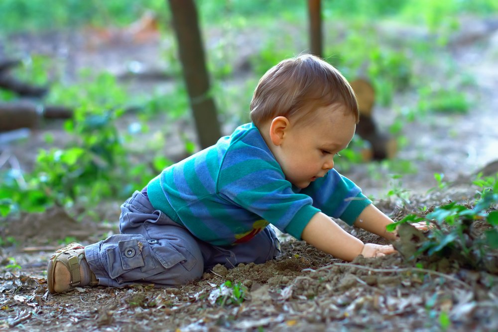 cute baby boy digging the ground in spring forest